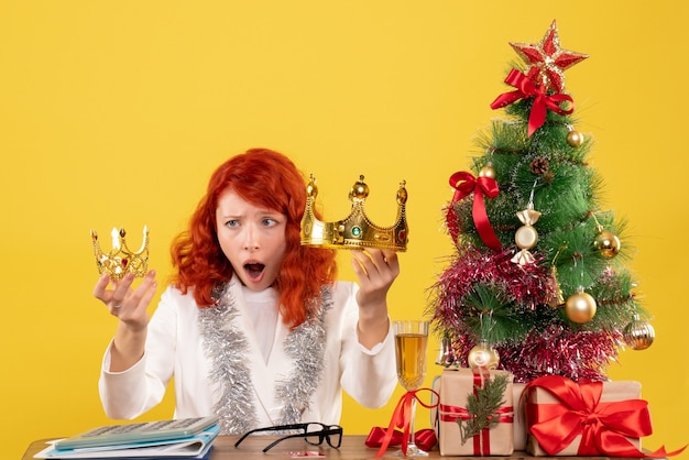 Vista frontal doctora sosteniendo coronas alrededor del árbol de Navidad y regalos