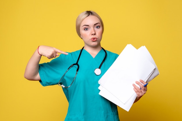 Vista frontal doctora sosteniendo diferentes papeles en el escritorio amarillo médico de salud pandémica hospital virus enfermera covid