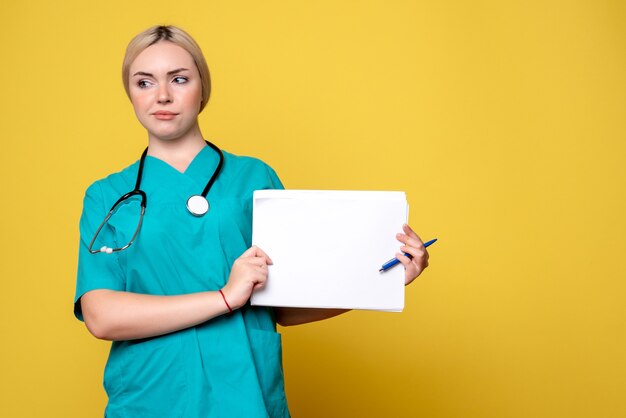 Vista frontal doctora sosteniendo diferentes papeles sobre el virus de escritorio amarillo médico de salud pandémica enfermera covid-19 hospital