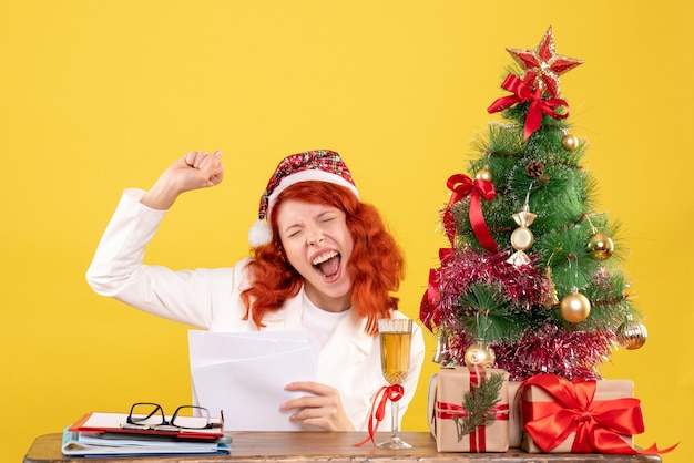 Vista frontal doctora sosteniendo documentos y sentado con regalos de navidad