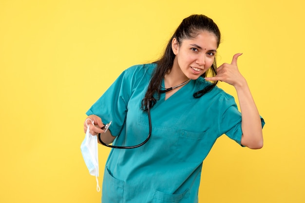 Vista frontal doctora sosteniendo estetoscopio haciendo llamarme gesto de teléfono permanente