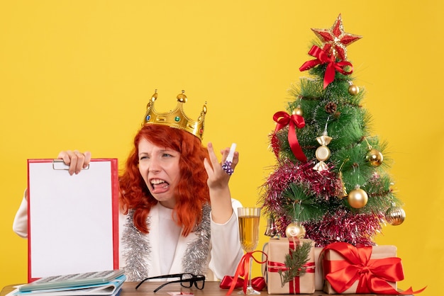 Vista frontal doctora sosteniendo la nota de archivo alrededor del árbol de Navidad y regalos