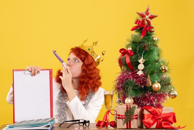 Vista frontal doctora sosteniendo la nota de archivo alrededor del árbol de Navidad y regalos