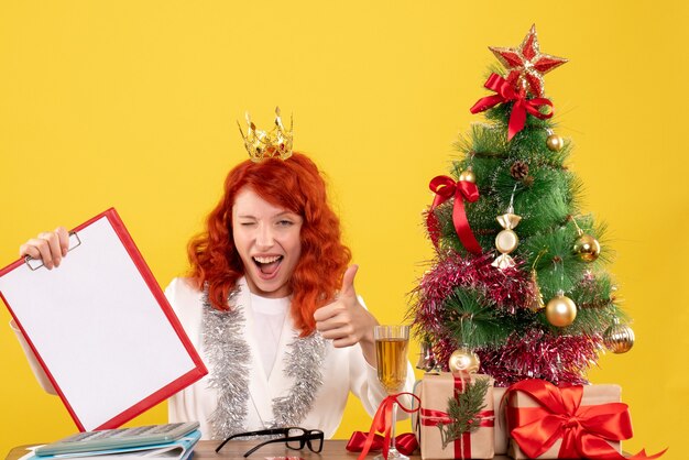 Vista frontal doctora sosteniendo la nota de archivo alrededor del árbol de Navidad y regalos