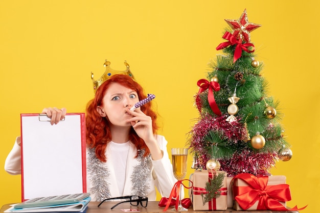Vista frontal doctora sosteniendo la nota de archivo alrededor del árbol de Navidad y regalos