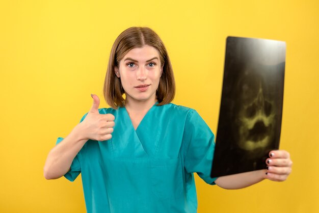 Vista frontal doctora sosteniendo radiografía en espacio amarillo