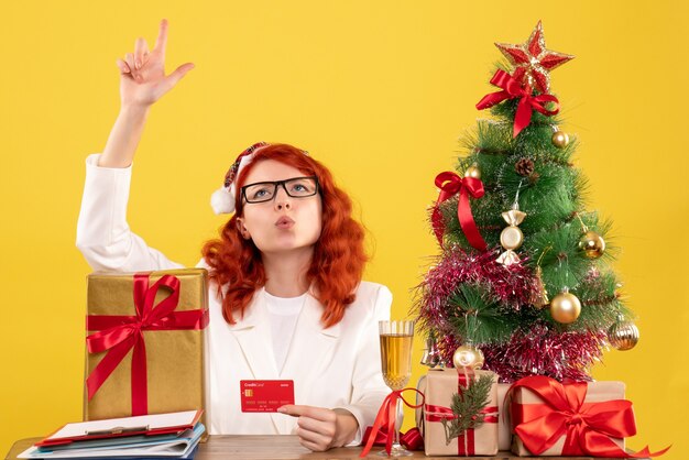 Vista frontal doctora sosteniendo tarjeta bancaria alrededor de árboles y regalos de Navidad