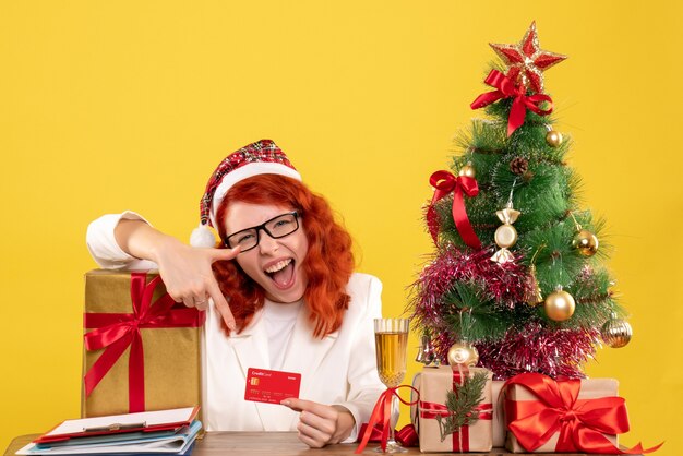 Vista frontal doctora sosteniendo tarjeta bancaria alrededor de árboles y regalos de Navidad