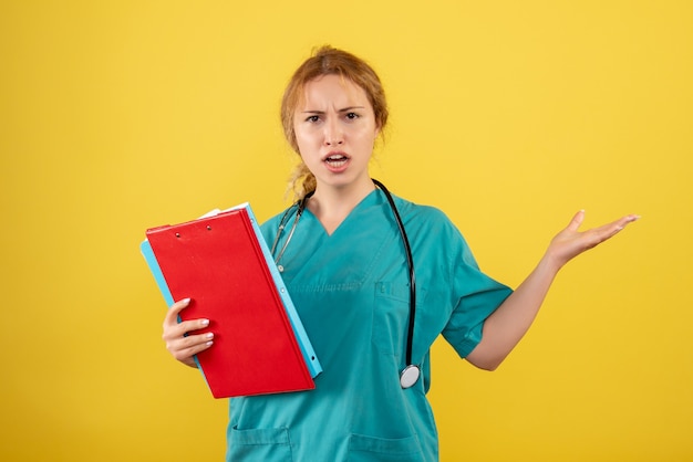 Vista frontal de la doctora en traje médico con análisis diferente en la pared amarilla