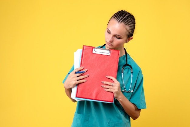 Foto gratuita vista frontal de la doctora en traje médico con análisis diferente en la pared amarilla