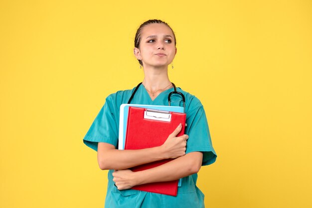 Vista frontal de la doctora en traje médico con análisis diferente en la pared amarilla