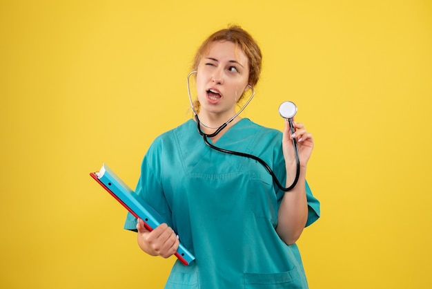 Vista frontal de la doctora en traje médico con análisis y estetoscopio en pared amarilla