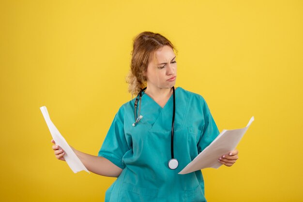 Vista frontal de la doctora en traje médico con análisis en pared amarilla