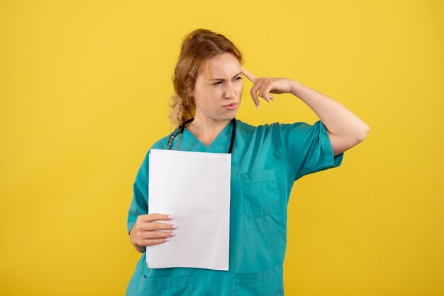 Vista frontal de la doctora en traje médico con análisis en pared amarilla