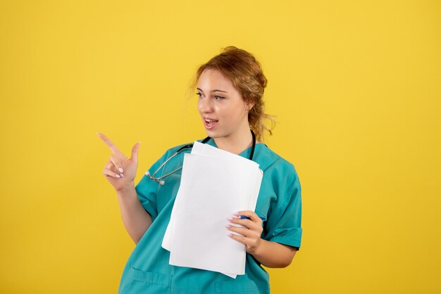 Vista frontal de la doctora en traje médico con análisis en pared amarilla