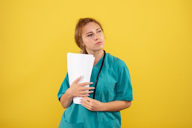 Vista frontal de la doctora en traje médico con análisis en pared amarilla