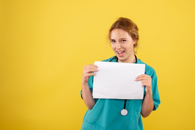 Vista frontal de la doctora en traje médico con análisis en pared amarilla