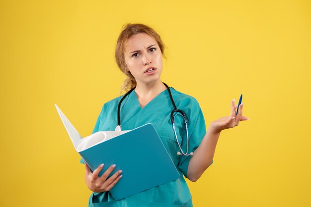 Vista frontal de la doctora en traje médico con análisis en pared amarilla