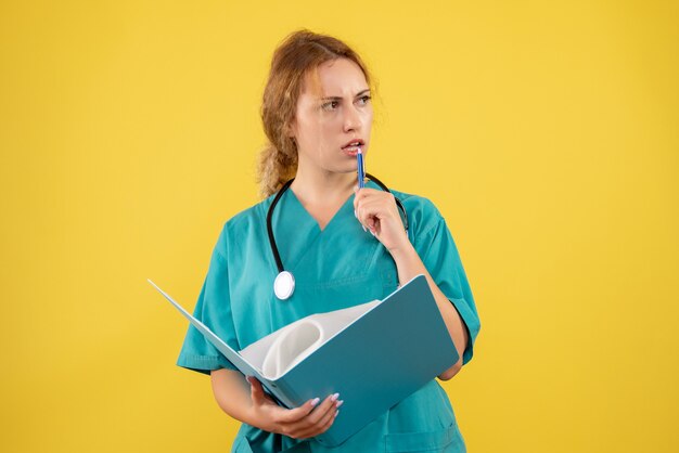 Vista frontal de la doctora en traje médico con análisis en pared amarilla