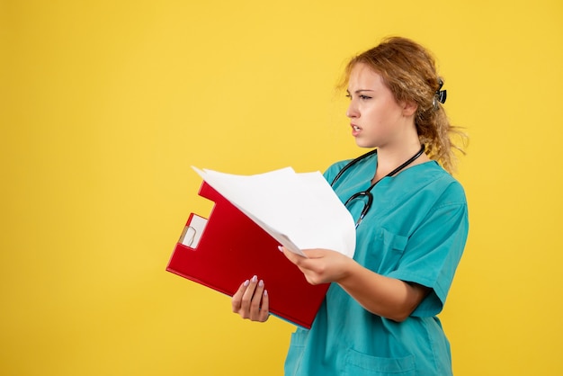 Vista frontal de la doctora en traje médico con análisis en pared amarilla