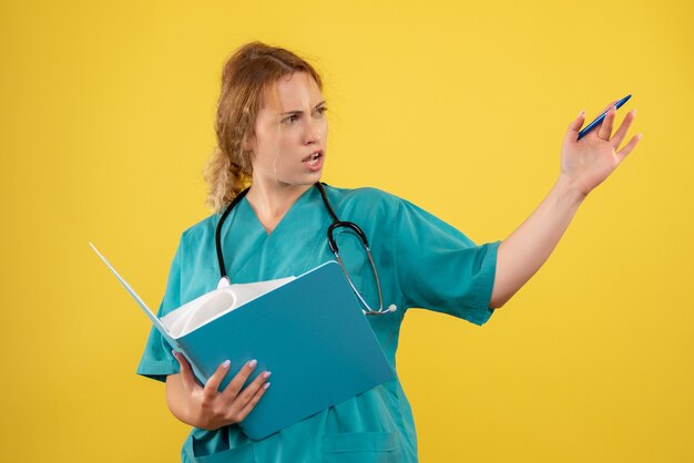 Vista frontal de la doctora en traje médico con análisis en pared amarilla