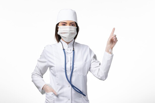 Vista frontal doctora en traje médico blanco estéril con máscara debido al coronavirus en la pared blanca enfermedad enfermedad enfermedad pandémica covid-