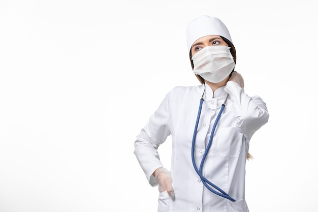 Vista frontal doctora en traje médico blanco estéril con máscara debido al coronavirus en la pared blanca enfermedad enfermedad pandemia covid-