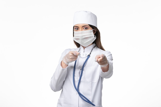 Vista frontal doctora en traje médico blanco estéril con máscara debido a coronavirus en la pared blanca enfermedad covid-enfermedad pandémica