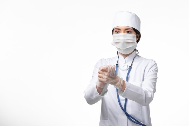 Vista frontal doctora en traje médico blanco estéril con máscara debido a covid- estrecharme la mano en la pared blanca enfermedad covid- enfermedad por virus pandémico