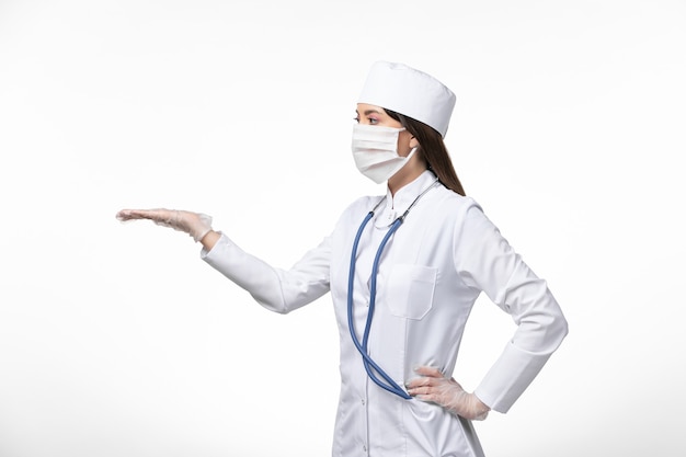 Vista frontal doctora en traje médico blanco estéril con máscara debido a covid- mostrando su mano en la pared blanca enfermedad covid- enfermedad por virus pandémico