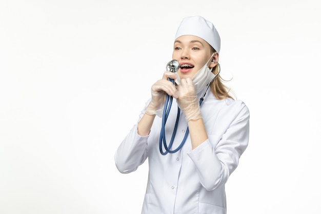 Vista frontal doctora en traje médico blanco con estetoscopio sobre escritorio blanco enfermedad covid-enfermedad pandémica