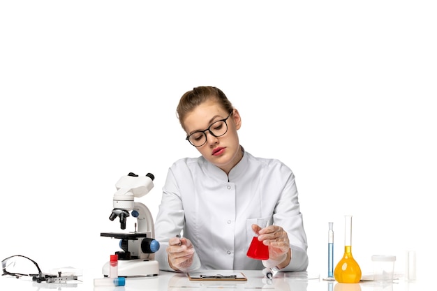 Vista frontal doctora en traje médico blanco con guantes sosteniendo matraz con solución en espacio en blanco claro