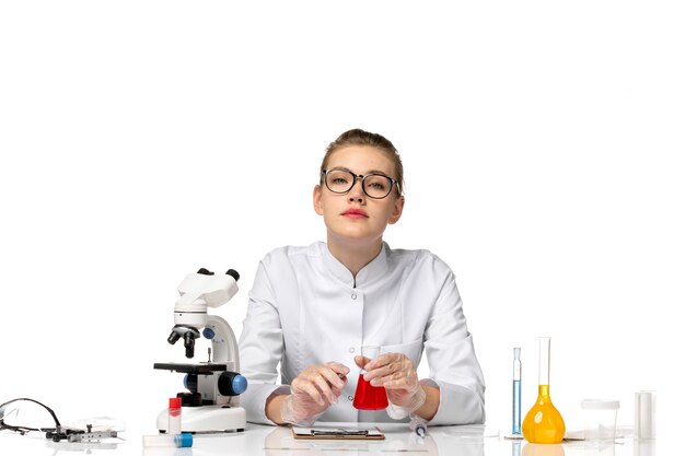 Vista frontal doctora en traje médico blanco con guantes sosteniendo matraz con solución en espacio en blanco