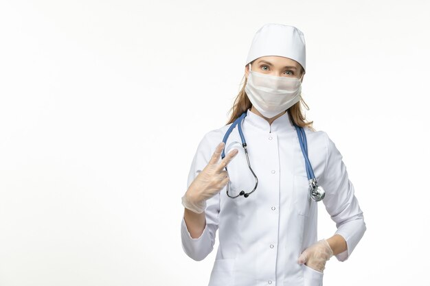 Vista frontal doctora con traje médico blanco y máscara como protección contra el coronavirus en la pared blanca enfermedad covid-enfermedad pandémica