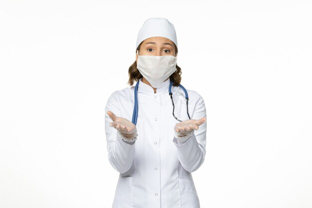 Vista frontal doctora en traje médico blanco y con máscara debido al coronavirus en la pared blanca virus enfermedad pandemia covid