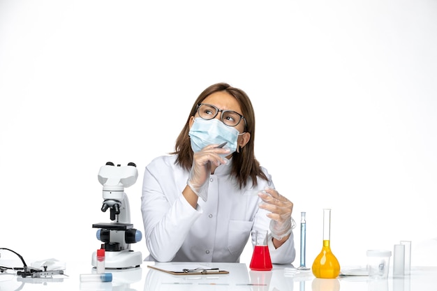 Vista frontal doctora en traje médico blanco con máscara debido al pensamiento covid en el espacio en blanco