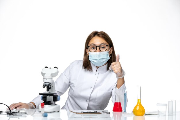 Vista frontal doctora en traje médico blanco con máscara debido a covid posando en un espacio en blanco