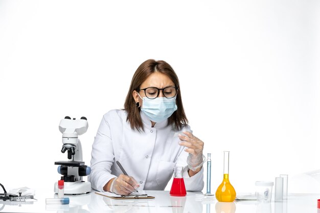 Vista frontal doctora en traje médico blanco con máscara debido a covid trabajando en espacios en blanco