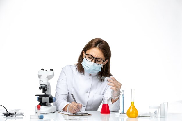 Vista frontal de la doctora en traje médico blanco con máscara debido a la escritura de covid en un espacio en blanco