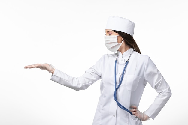 Vista frontal doctora en traje médico blanco con una máscara debido a la pandemia en la pared de color blanco claro medicina virus pandémico covid-