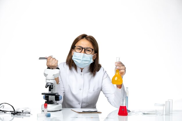 Vista frontal doctora en traje médico blanco con máscara debido a que covid trabaja con soluciones escribiendo en espacios en blanco