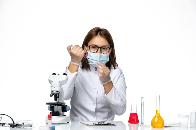 Foto gratuita vista frontal doctora en traje médico blanco con máscara debido a que covid trabaja con soluciones en espacios en blanco claro