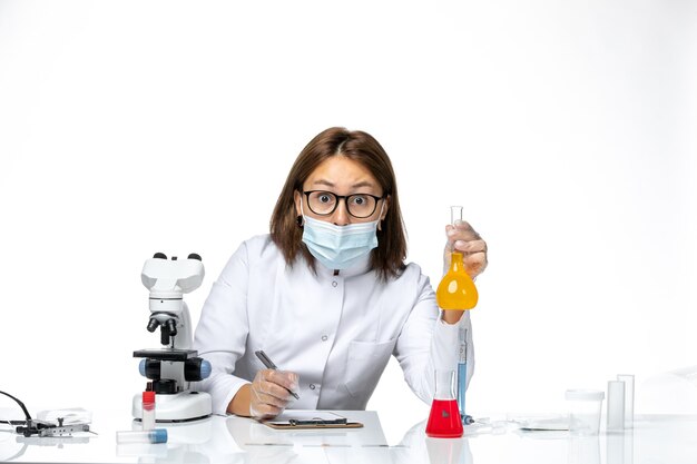 Vista frontal doctora en traje médico blanco con máscara debido a que covid trabaja con soluciones en espacios en blanco