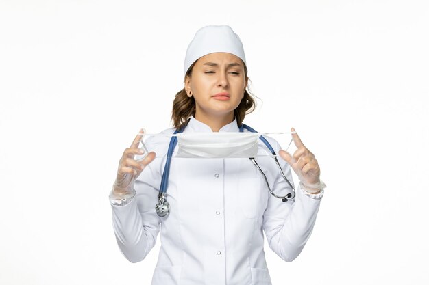 Vista frontal doctora en traje médico blanco con máscara en la pared blanca enfermedad pandémica medicina aislamiento de virus