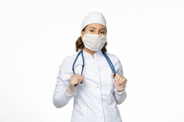 Vista frontal doctora en traje médico blanco y máscara en la pared blanca luz enfermedad del virus de la pandemia enfermedad medicina