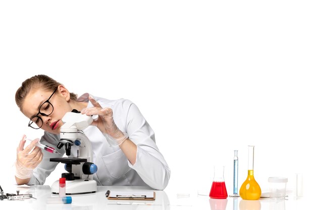 Vista frontal doctora en traje médico blanco con microscopio en un espacio en blanco claro