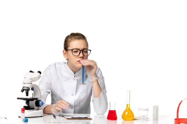 Vista frontal doctora en traje médico blanco trabajando con soluciones en el espacio en blanco claro