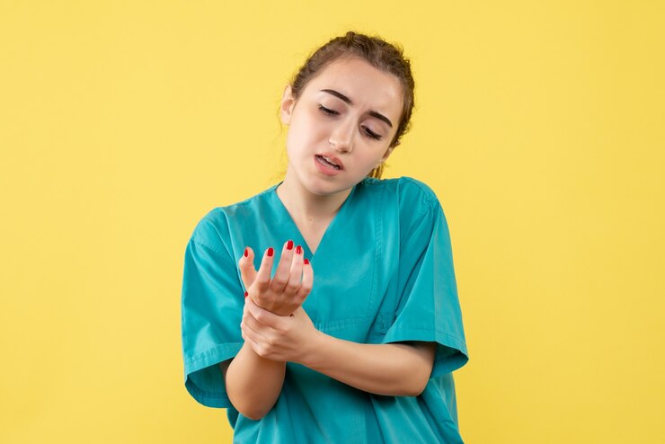 Vista frontal de la doctora en traje médico con brazo herido en pared amarilla