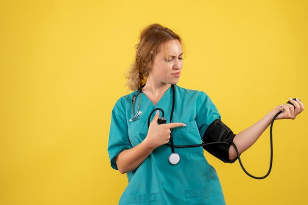 Vista frontal de la doctora en traje médico comprobando su presión sobre la pared amarilla