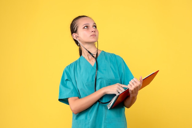 Vista frontal de la doctora en traje médico con estetoscopio y análisis en pared amarilla